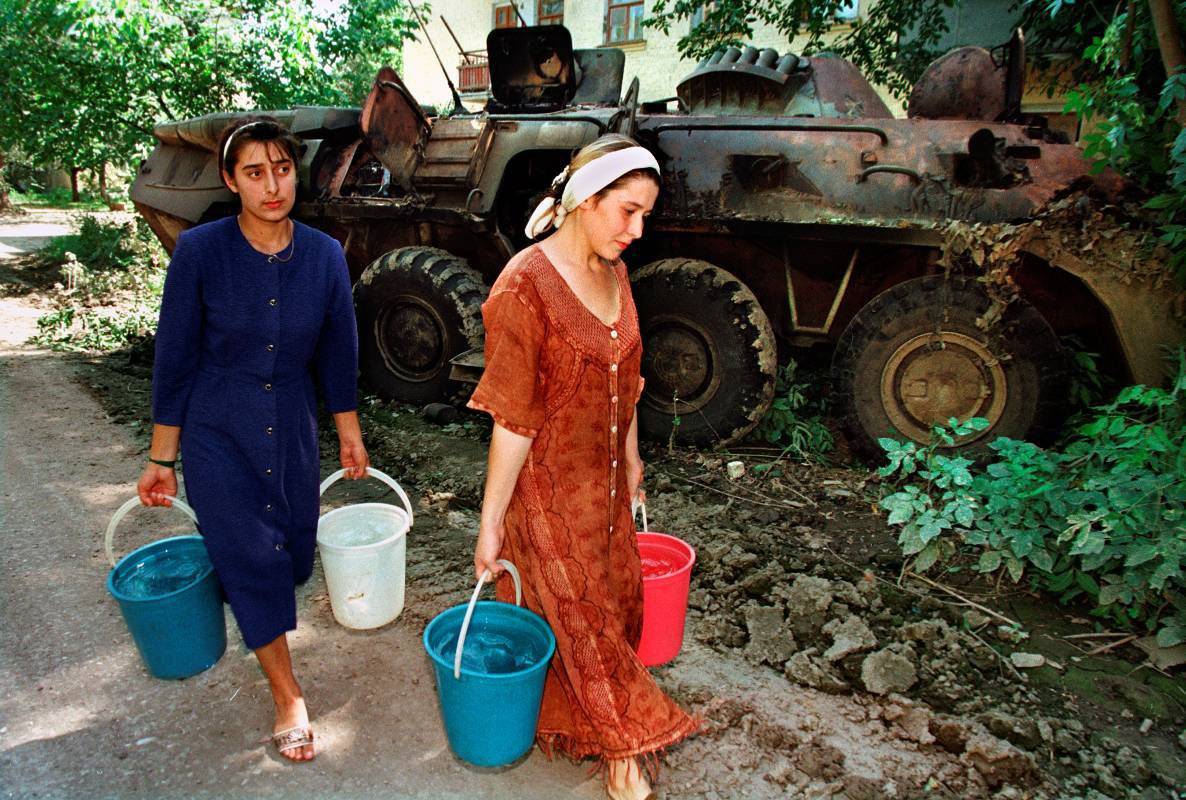 Женщины несут воду из колодца, проходя мимо уничтоженного БТР-80 федеральных войск, Чечня, 1995 г.