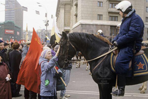 Мальчик с флагом СССР и свёртком, запихнутым в карман куртки, гладит коня сотрудника милиции. Москва, период митингов весны 1993 г.
