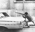 Боец ведет огонь скрываясь за автомобилем на улице Бейрута. Ливан. Гражданская война в Ливане. Декабрь 1975 г..jpg