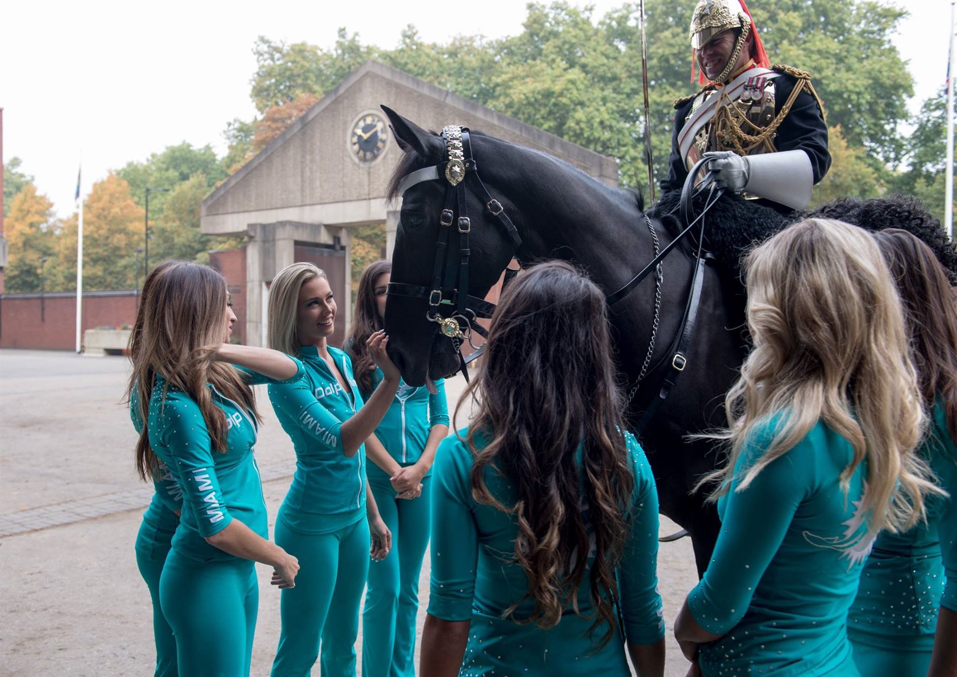 Девушки из команды чирлидинга "Miami Dolphins" рассматривают лошадь и кавалериста полка Дворцовой кавалерии, Лондон, 27 сентября 2017 г.