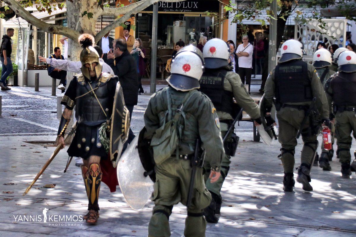 Реконструктор в доспехах древнегреческого гоплита проходит мимо современных греческих полицейских во время массовых беспорядков, Афины, 26 октября 2018 г.