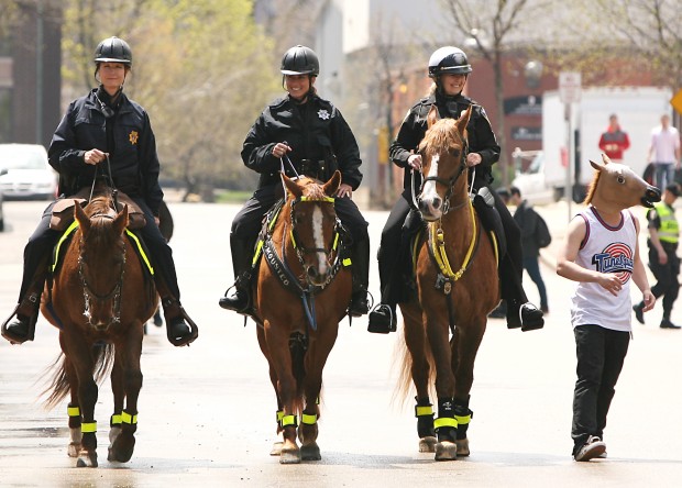 Студент в маске в виде лошадиной головы проходит мимо трех конных полицейских, патрулирующих город Западный Бенд, США, 2013 г.