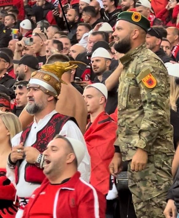 Албанец в униформе армии освобождения Косова на футбольном матче национальной сборной Албании против Италии, Дортмунд, Германия, 15 июня 2024 г. Справа от него болельщик одет в национальный албанский костюм со шлемом Скандербега.