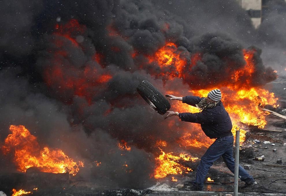 Активист Майдана добрасывает еще одну покрышку в горящую баррикаду из шин, Киев, январь 2014 г.