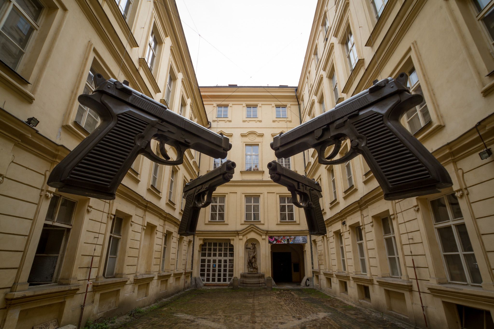 Арт-инсталляция "Оружие", представляющая собой четыре огромных пистолета Beretta 92, подвешенные в воздухе. Автор чешский художник Давида Чёрный, 2012 г.