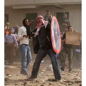 An anti-government protester uses a road sign as a shield as he throws stones.jpg