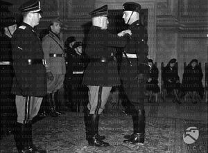 Mussolini appunta la medaglia al valore sul petto di un Moschettiere, dietro di lui Vidussoni, D'Havet e Galbiati 11.02.1942.jpg