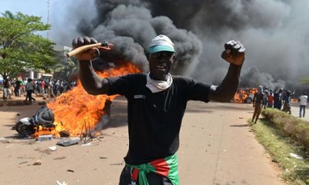 Protesters stand outside the parliament in Ouagadougou as cars and documents burn outside.jpeg