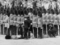 Медики помогают солдату Почетного караула, упавшему в обморок из-за жары на репетиции церемонии выноса знамени, Лондон, 1 июня 1963.jpg